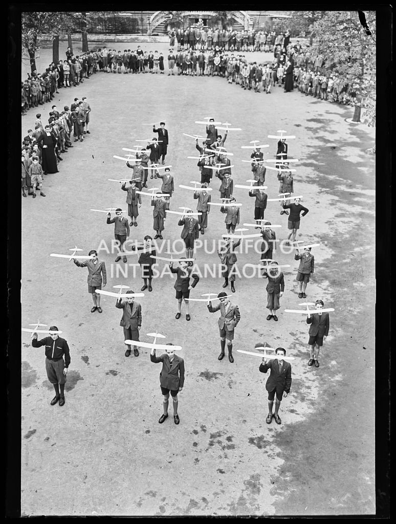 Ragazzi mostrano modellini di aeroplano, nel cortile di una scuola, al pubblico dei compagni e a religiosi