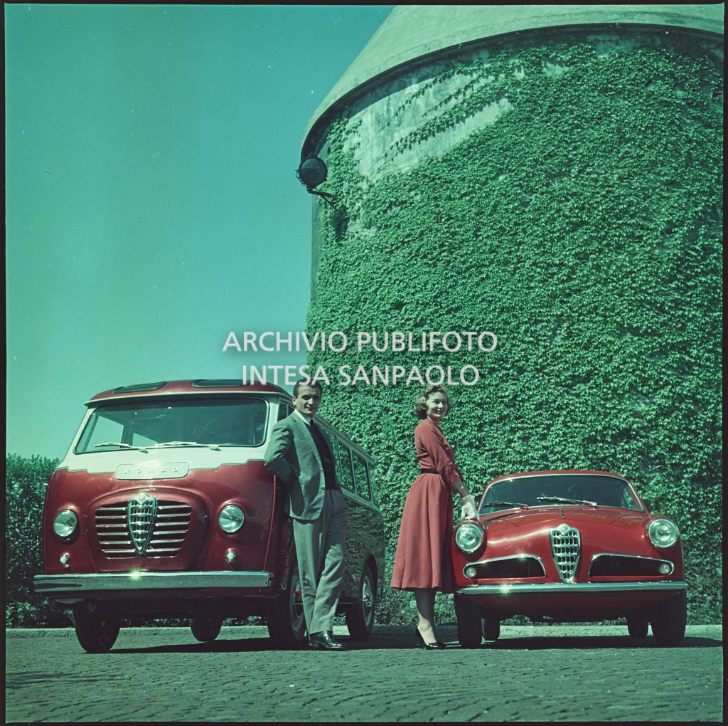 Alfa Romeo rossa 1900, e furgoncino Romeo rosso e bianco. Accanto alle due vetture un uomo e una donna