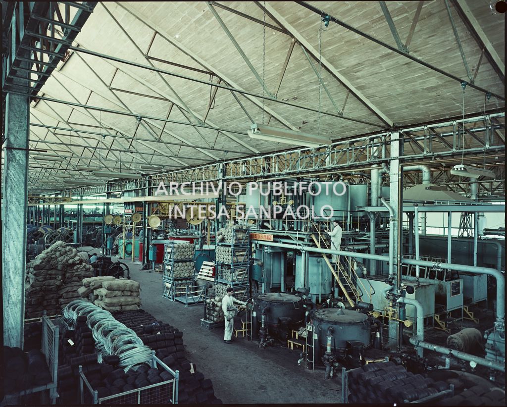 Interno dello stabilimento Pirelli con macchinari, materie prime ed operai al lavoro