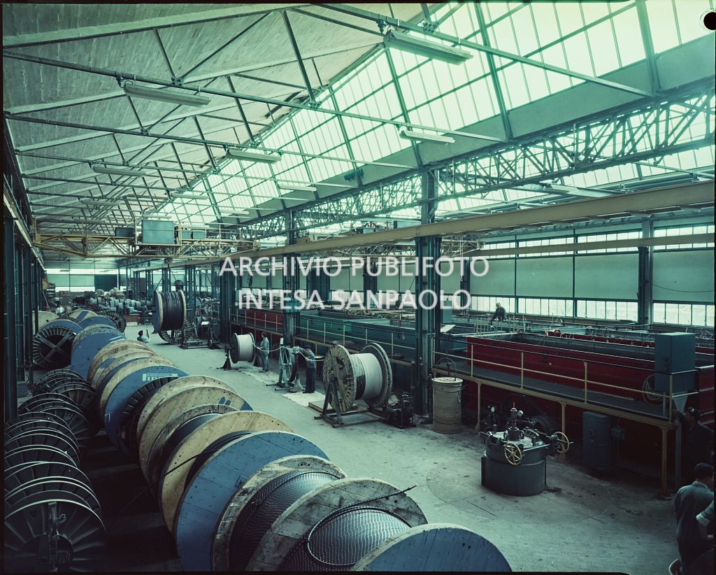 Interno dello stabilimento Pirelli con macchinari, materie prime ed operai al lavoro
