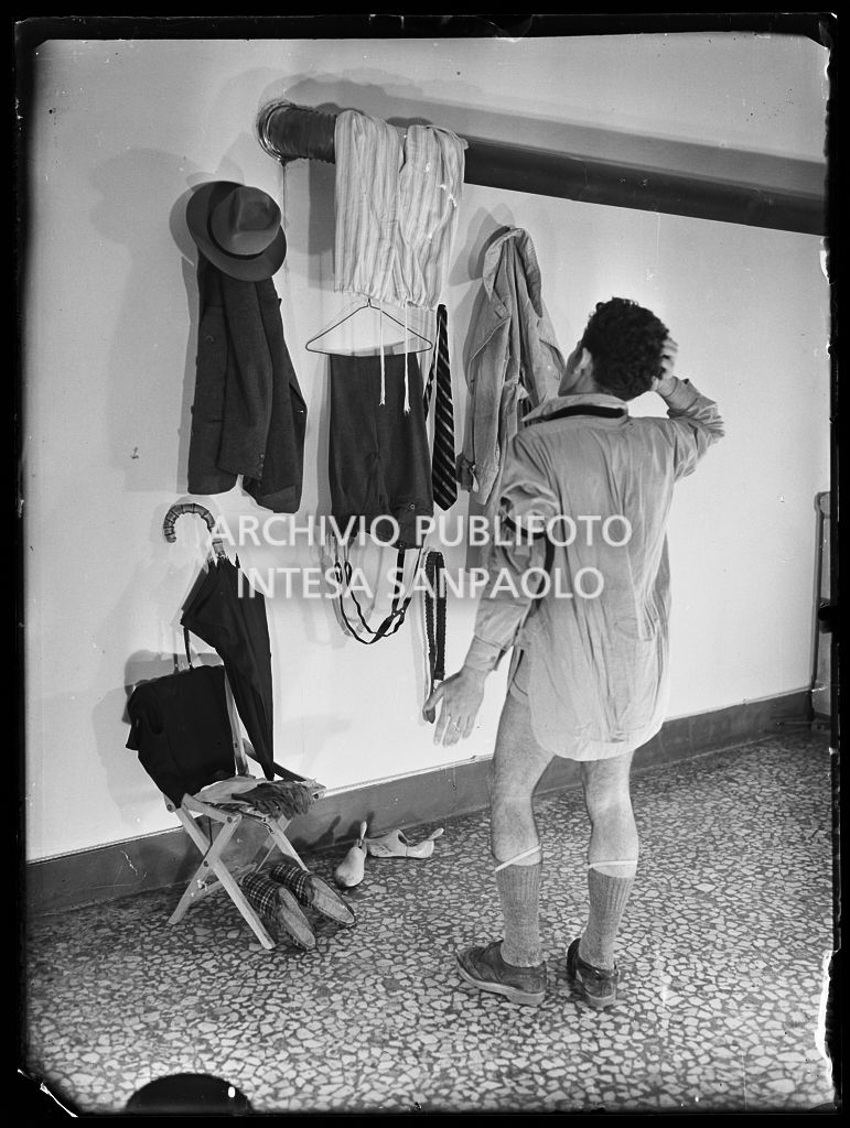 Un uomo si veste scegliendo tra gli abiti appesi alla parete