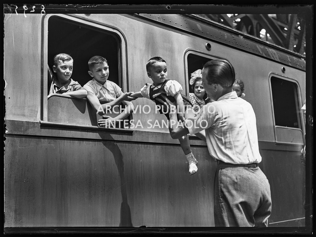 Due bambini sul treno salutano il fratellino e il padre attraverso il finestrino
