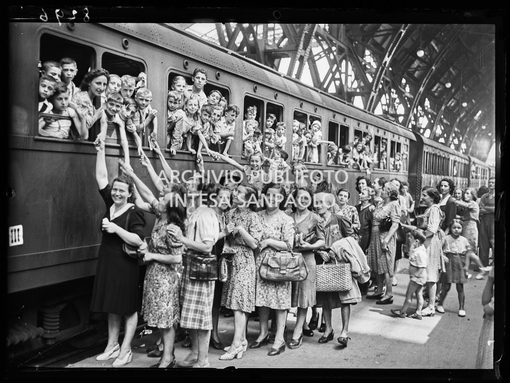 Bambini, in partenza per la colonia estiva, affacciati al finestrino del treno, alla Stazione Centrale a Milano, salutano le mamme emozionate sulla banchina