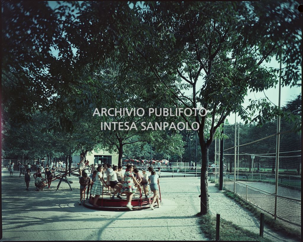 Bambini giocano su una giostra girevole e un dondolo in un parco di Milano
