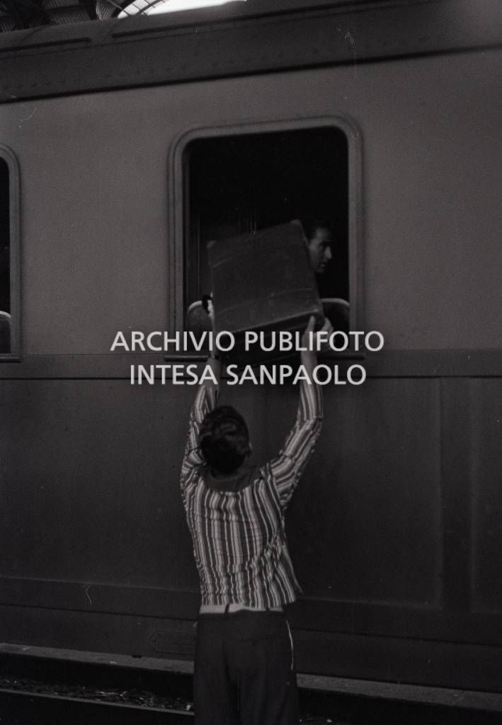 Immigrati dal Sud Italia alla Stazione Centrale di Milano: un uomo carica (o scarica) una valigia attraverso un finestrino di un treno