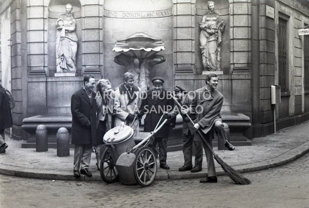 Line Renaud a braccetto con Renato Carosone (a sinistra) in posa, tra gli altri, con due netturbini e Paolo Poli (a destra), in via Andegari all'angolo con via Romagnosi a Milano<br>709203/1