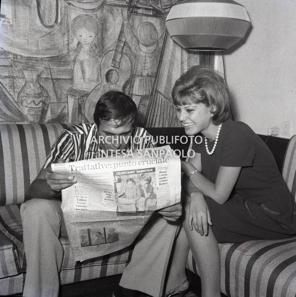 Adriano Celentano e Claudia Mori, seduti sul divano, leggono insieme il quotidiano  "Il Giorno" su cui è pubblicata una loro fotografia