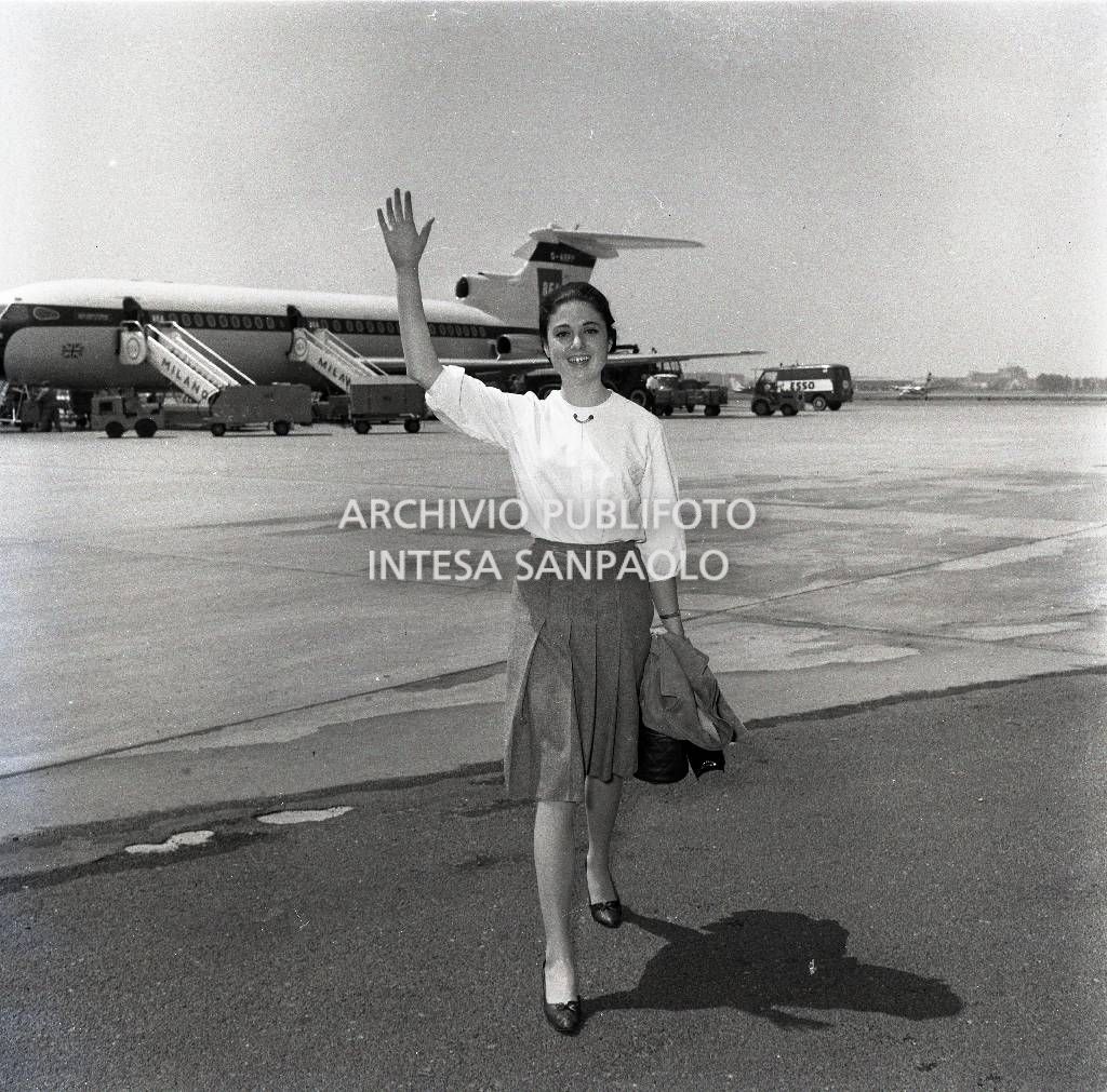 Gigliola Cinquetti saluta al suo arrivo all'aeroporto di Milano Linate; alle sue spalle un aeroplano in pista<br>722906/11