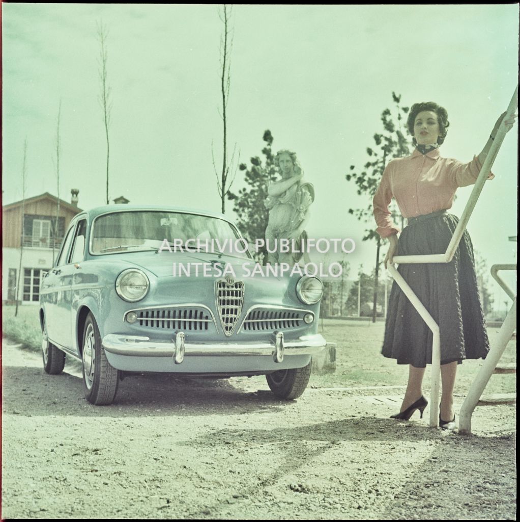 Alfa Romeo Giulietta berlina azzurra  in un giardino con accanto una modella