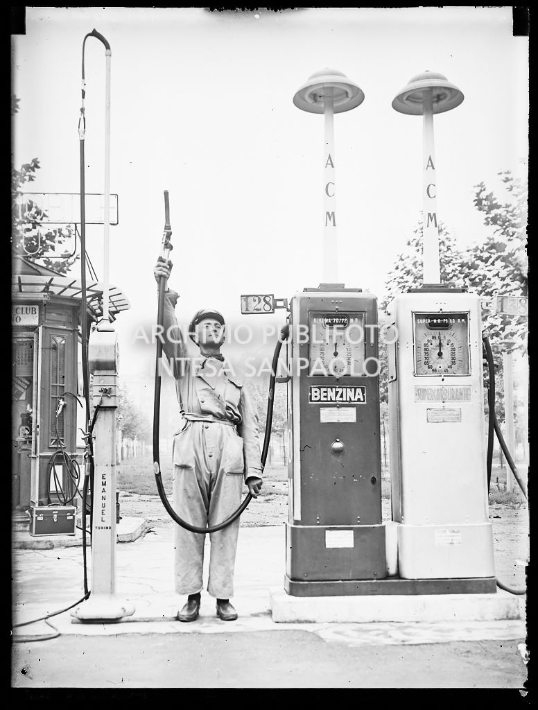 Addetto a una stazione di rifornimento dell'Automobile Club di Milano ritratto con la pompa di benzina sollevata