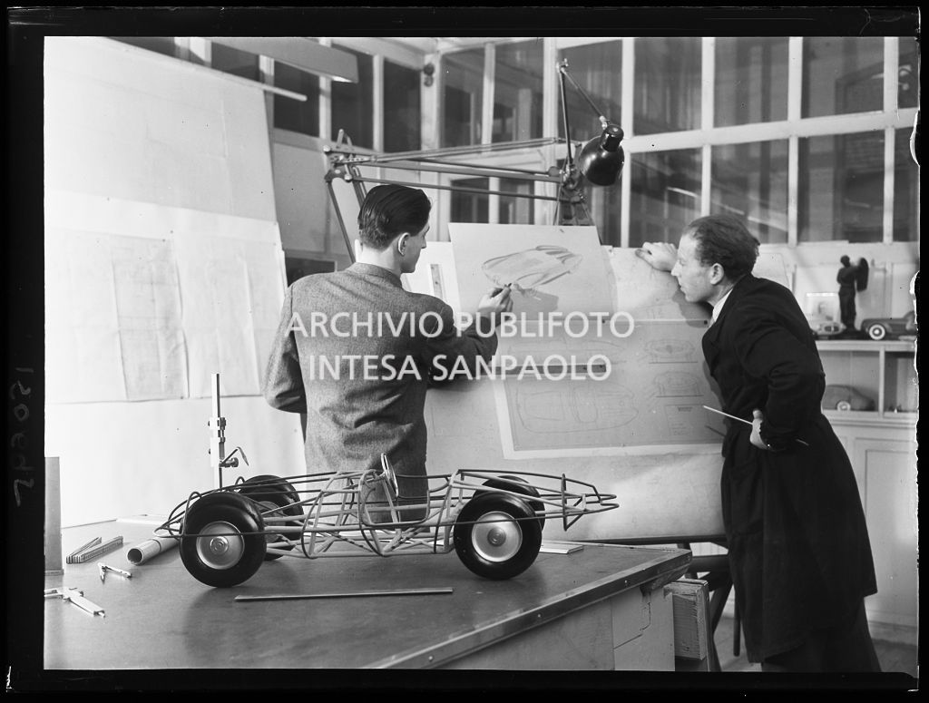 Due uomini lavorano allo schizzo del prototipo dell'automobile C52 "Disco Volante" all'Alfa Romeo; in primo piano il modello del telaio