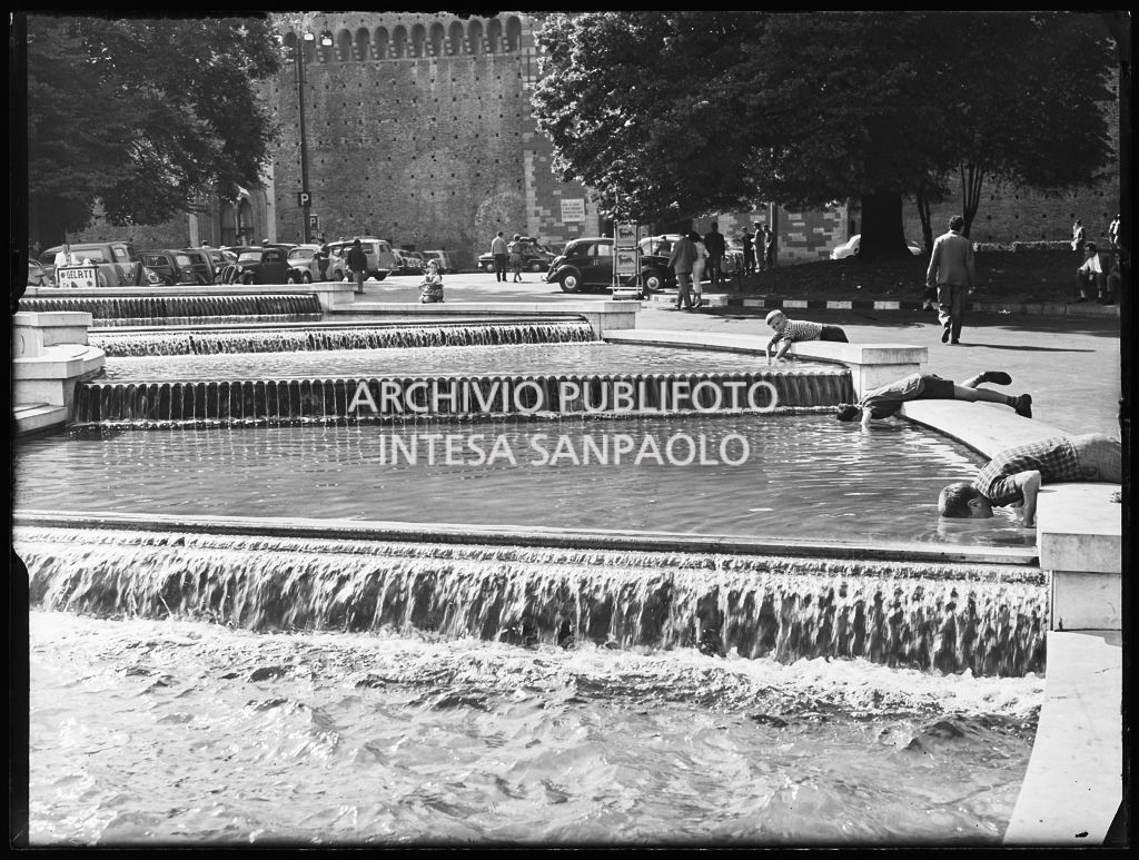 Tre bambini giocano al bordo della fontana davanti al Castello Sforzesco