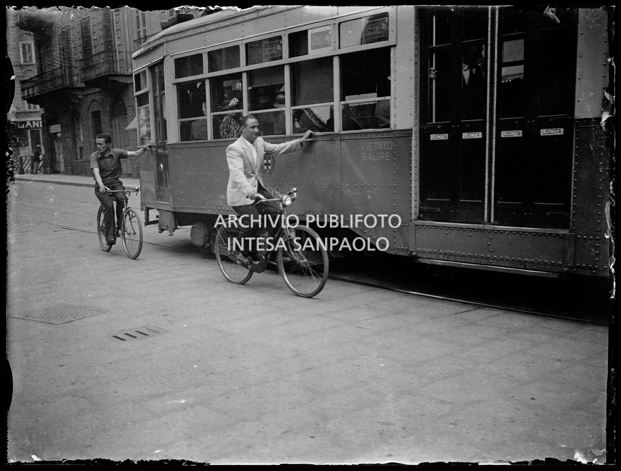 Due uomini in bicicletta si fanno trainare da un tram a Milano