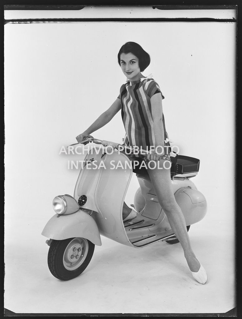 Una modella posa, su limbo bianco, in sella a una Vespa 125 VN2T