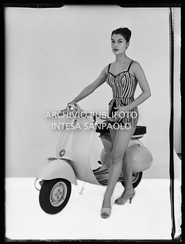 Una modella posa, su limbo bianco, accanto a una Vespa 125 VN2T