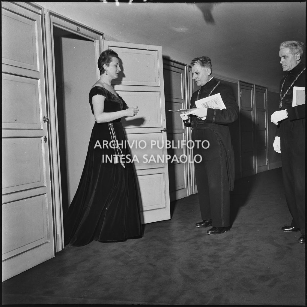 La contessa Franca Belgioioso, sulla soglia del palco al Teatro alla Scala,  con le maschere che le porgono il libretto di sala, in occasione della serata inaugurale della stagione lirica 1952-1953 con l'opera "Macbeth" di Giuseppe Verdi diretta da Victor de Sabata, con la regia di Carl Ebert