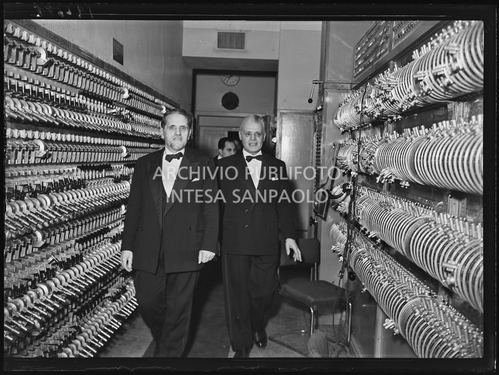 Il senatore Teodoro Bubbio accompagnato da Antonio Ghiringhelli, sovrintendente del Teatro alla Scala,  nei locali di controllo attrezzature di scena, dietro alla quinte, la sera dell'inaugurazione della stagione lirica 1953-1954 con l'opera "La Wally", di Alfredo Catalani, diretta da Carlo Maria Giulini, con la regia di Tatiana Pavlova