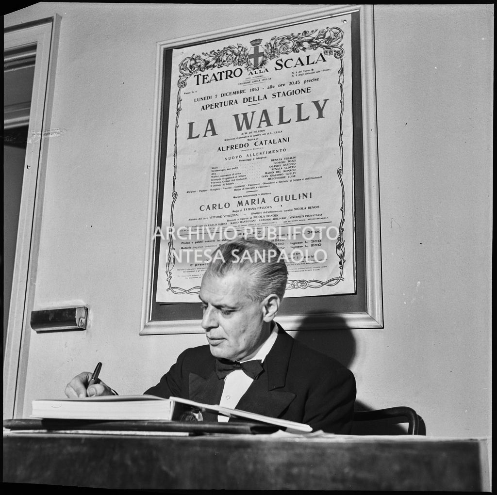 Il sovrintendente del Teatro alla Scala, Antonio Ghiringhelli, in teatro la sera dell'inaugurazione della stagione lirica 1953-1954 con l'opera "La Wally", di Alfredo Catalani, diretta da Carlo Maria Giulini, con la regia di Tatiana Pavlova; alle sue spalle la locandina dell'opera.