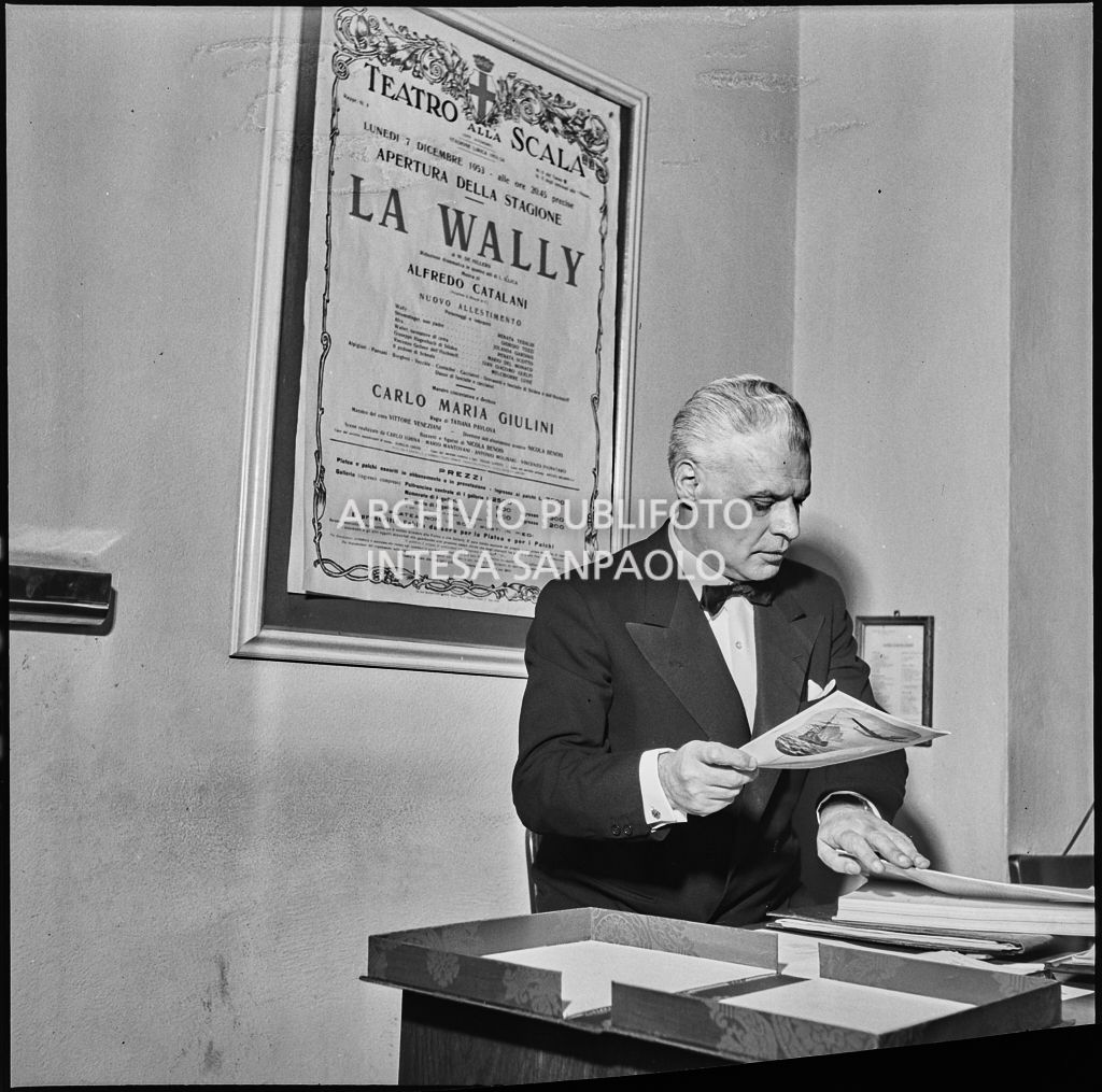 Il sovrintendente del Teatro alla Scala, Antonio Ghiringhelli, in teatro la sera dell'inaugurazione della stagione lirica 1953-1954 con l'opera "La Wally", di Alfredo Catalani, diretta da Carlo Maria Giulini, con la regia di Tatiana Pavlova; alle sue spalle la locandina dell'opera
