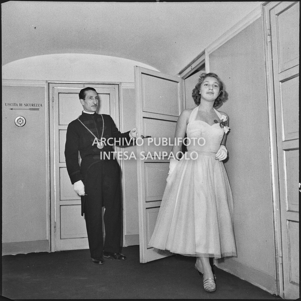 Una maschera del Teatro alla Scala tiene aperta la porta del palco a Marina Vitali la sera della  inaugurazione della stagione lirica 1954-1955 con l'opera "La Vestale", di Gaspare Spontini, diretta da Antonino Votto, con la regia di Luchino Visconti