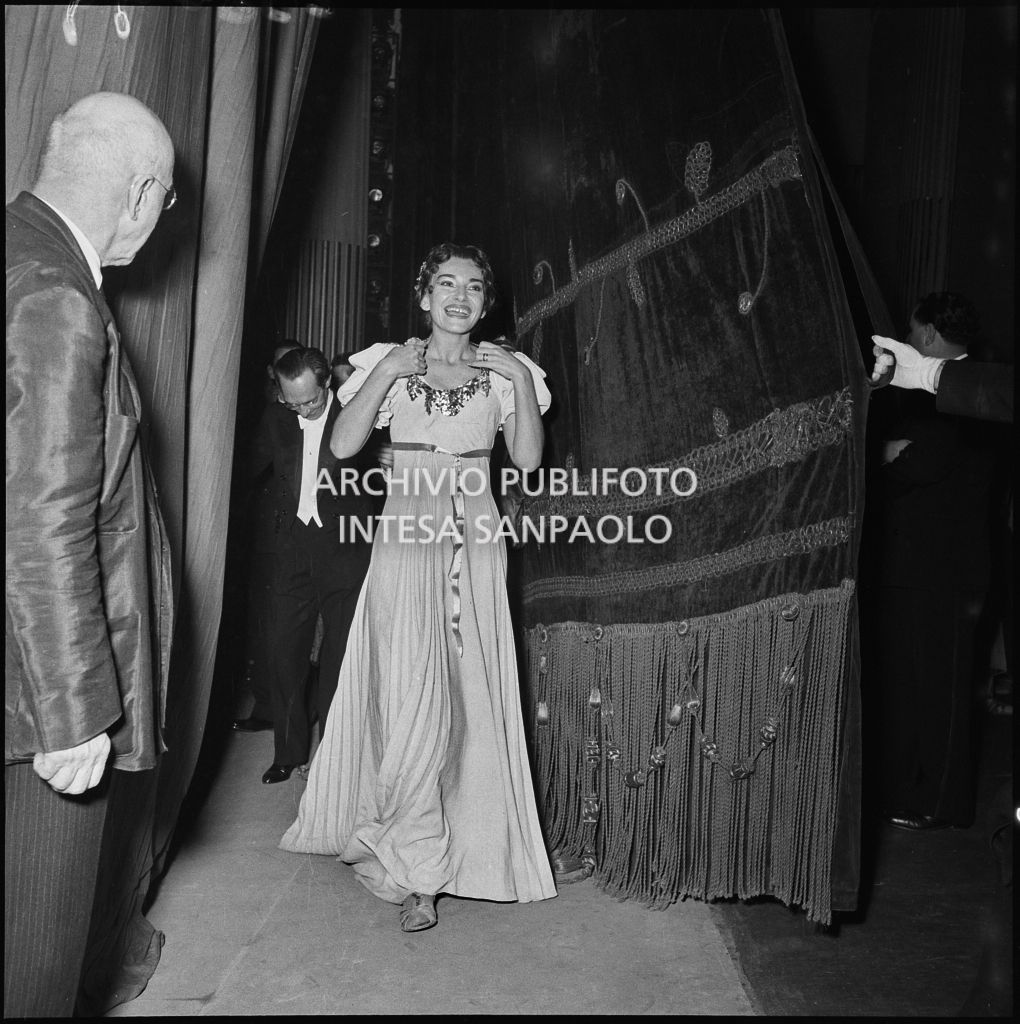 La soprano Maria Callas, in costume di scena, seguita dal direttore d'orchestra Antonino Votto, dietro alle quinte in occasione della serata inaugurale della stagione lirica 1954-1955 del Teatro alla Scala con l'opera "La Vestale", di Gaspare Spontini, diretta dallo stesso Votto e con la regia di Luchino Visconti