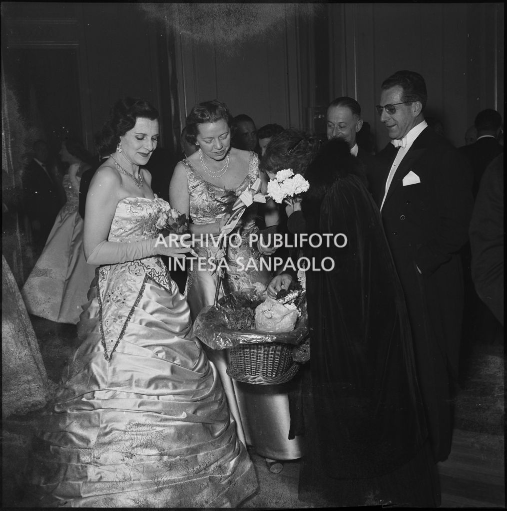 Da sinistra, la signora Bracco e la signora Rosenberg Colorni acquistano dei fiori nel foyer del Teatro alla Scala in occasione della serata inaugurale della stagione lirica 1955-1956 con l'opera "Norma" di Vincenzo Bellini, diretta da Antonino Votto con la regia di Margherita Wallmann