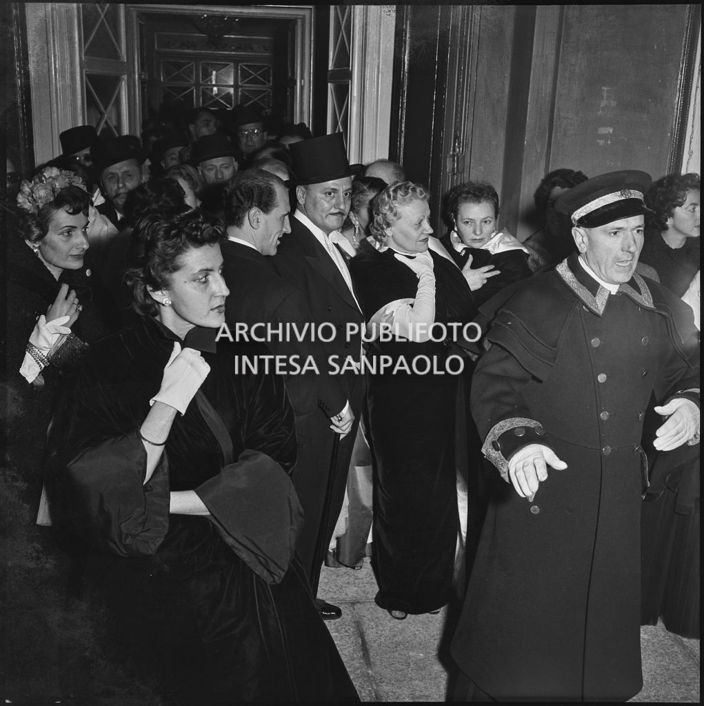 Lo stilista Pierre Balmain, tra la folla di spettatori, nella galleria delle carrozze del Teatro alla Scala la sera dell'inaugurazione della stagione lirica 1955-1956 con l'opera "Norma" di Vincenzo Bellini, diretta da Antonino Votto con la regia di Margherita Wallmann