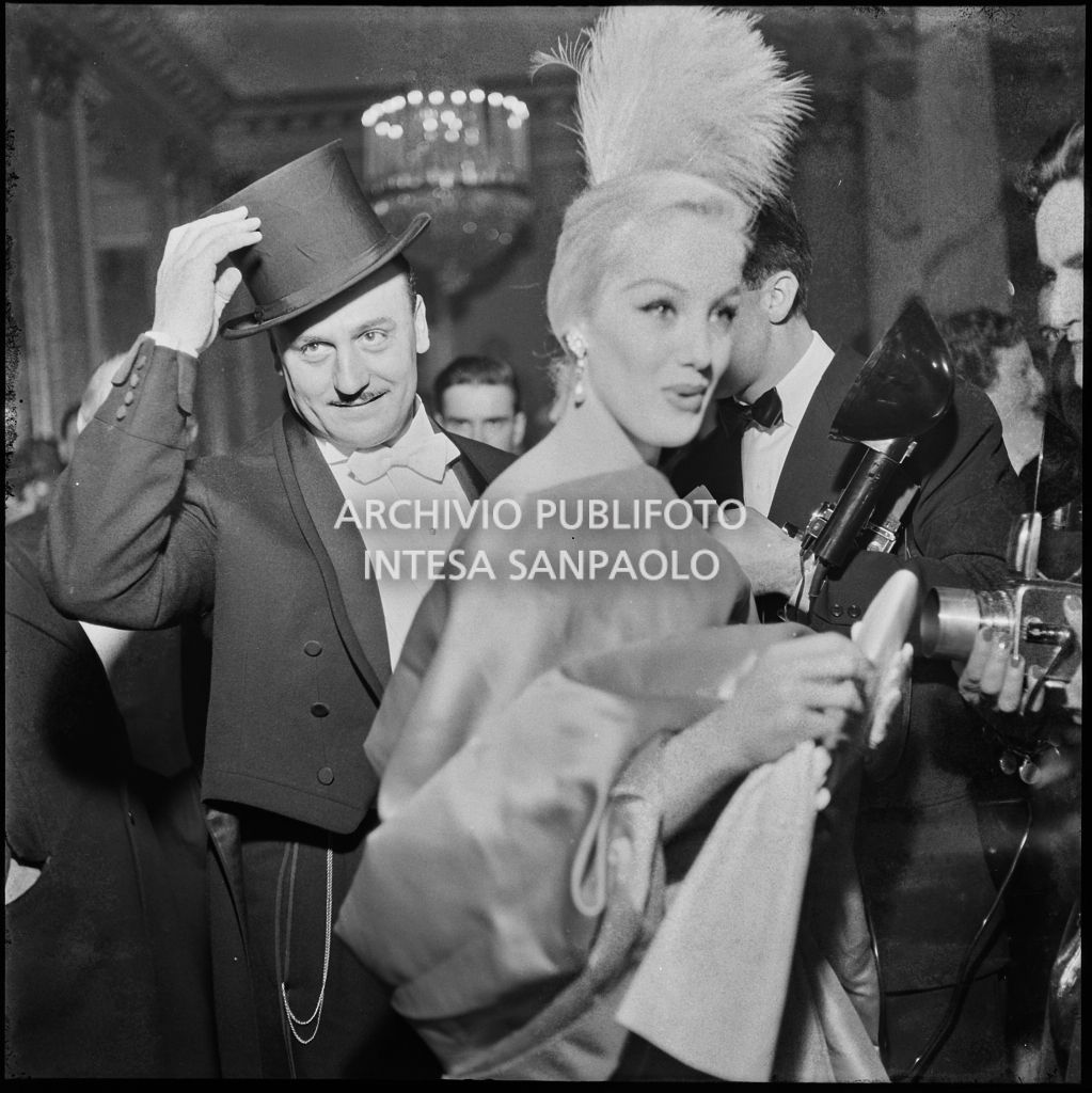Lo stilista Pierre Balmain e Barbara Balmain nel foyer del Teatro alla Scala in occasione della serata inaugurale della stagione lirica 1956-1957 con l'opera "Aida" di Giuseppe Verdi, diretta da Antonino Votto con la regia di Franco Enriquez