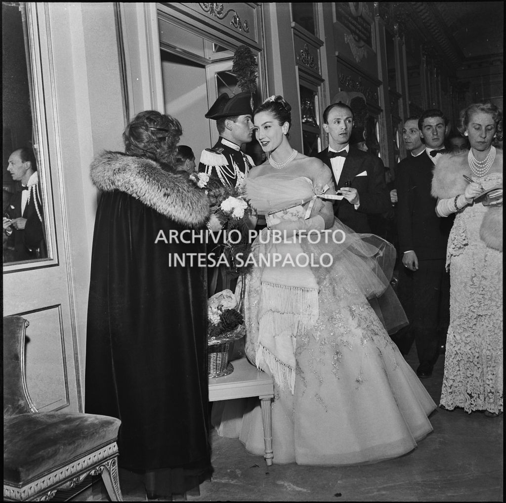 Giuliana Brenner acquista un mazzo di fiori nel foyer del Teatro alla Scala in occasione della serata inaugurale della stagione lirica 1956-1957 con l'opera "Aida" di Giuseppe Verdi, diretta da Antonino Votto con la regia di Franco Enriquez
