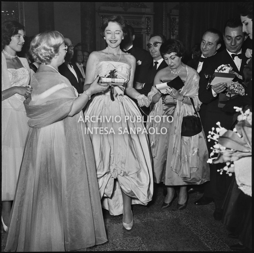 Jole Veneziani consegna un pacchetto alla contessa Anna Sogno al Teatro alla Scala in occasione della serata inaugurale della stagione lirica 1957-1958 con l'opera "Un ballo in maschera", di Giuseppe Verdi, diretta da Gianandrea Gavazzeni e la regia di Margherita Wallmann