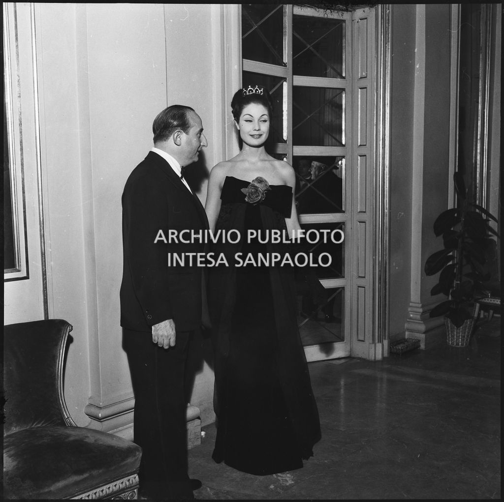 Eletta Polvani in compagnia di un uomo nel foyer del Teatro alla Scala in occasione della serata inaugurale della stagione lirica 1957-1958 con l'opera "Un ballo in maschera", di Giuseppe Verdi, diretta da Gianandrea Gavazzeni e la regia di Margherita Wallmann