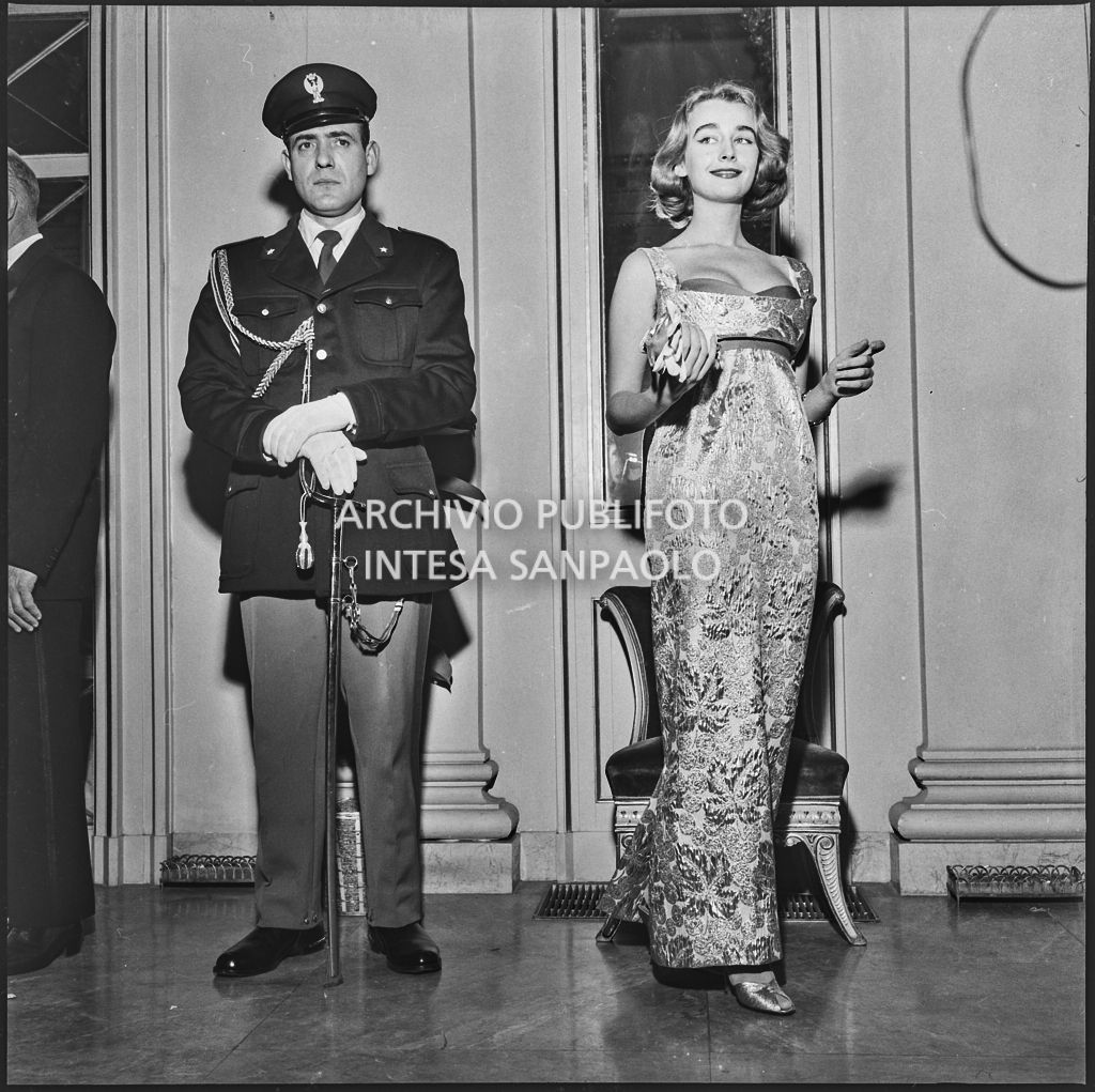 Beatrice Faccioli, in posa accanto ad un carabiniere, nel foyer del Teatro alla Scala in occasione della serata inaugurale della stagione lirica 1957-1958 con l'opera "Un ballo in maschera", di Giuseppe Verdi, diretta da Gianandrea Gavazzeni e la regia di Margherita Wallmann