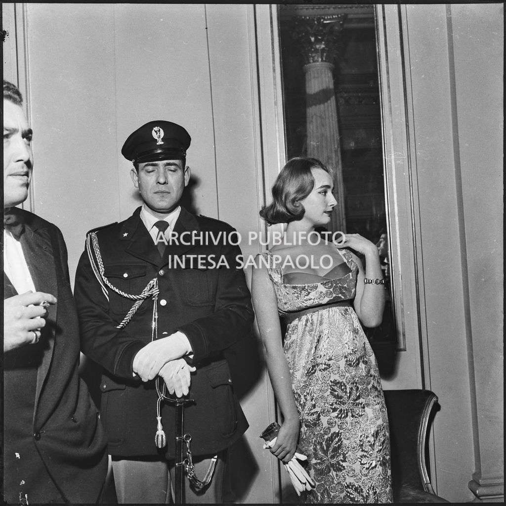 Beatrice Faccioli in posa accanto ad un poliziotto nel foyer del Teatro alla Scala in occasione della serata inaugurale della stagione lirica 1957-1958 con l'opera "Un ballo in maschera", di Giuseppe Verdi, diretta da Gianandrea Gavazzeni e la regia di Margherita Wallmann