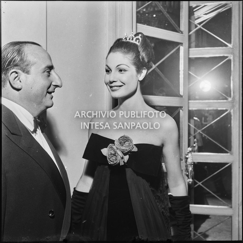 Eletta Polvani in compagnia di un uomo nel foyer del Teatro alla Scala in occasione della serata inaugurale della stagione lirica 1957-1958 con l'opera "Un ballo in maschera", di Giuseppe Verdi, diretta da Gianandrea Gavazzeni e la regia di Margherita Wallmann