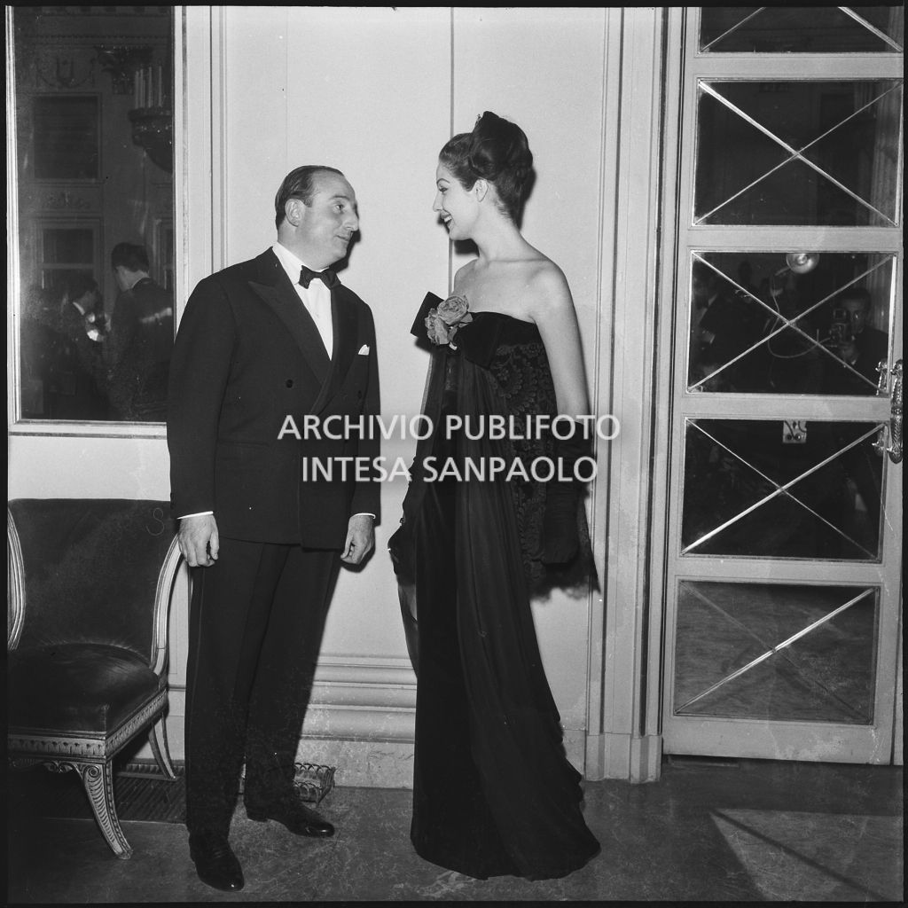 Eletta Polvani in compagnia di un uomo nel foyer del Teatro alla Scala in occasione della serata inaugurale della stagione lirica 1957-1958 con l'opera "Un ballo in maschera", di Giuseppe Verdi, diretta da Gianandrea Gavazzeni e la regia di Margherita Wallmann