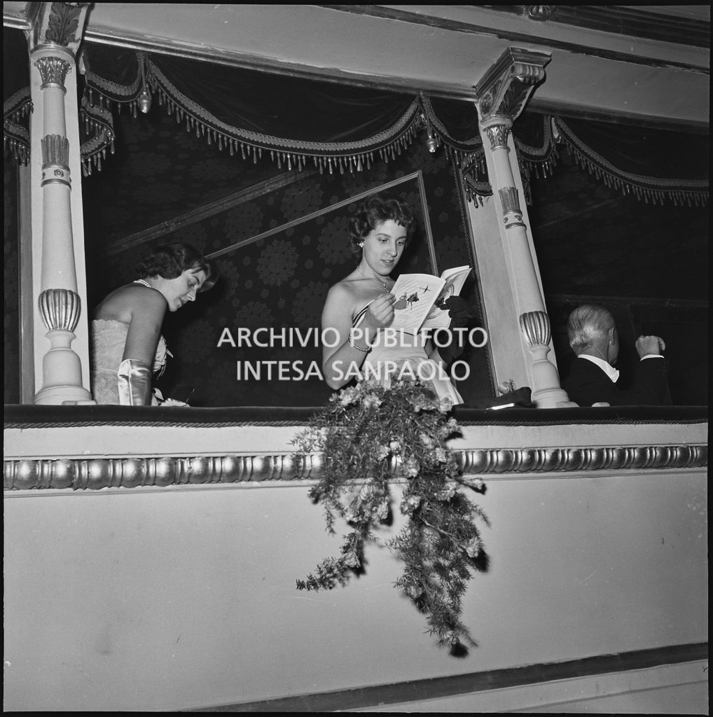 Una ragazza legge il libretto di sala in un palco del Teatro alla Scala, in occasione della serata inaugurale della stagione lirica 1955-1956 con l'opera "Norma" di Vincenzo Bellini, diretta da Antonino Votto, con la regia di Margherita Wallmann