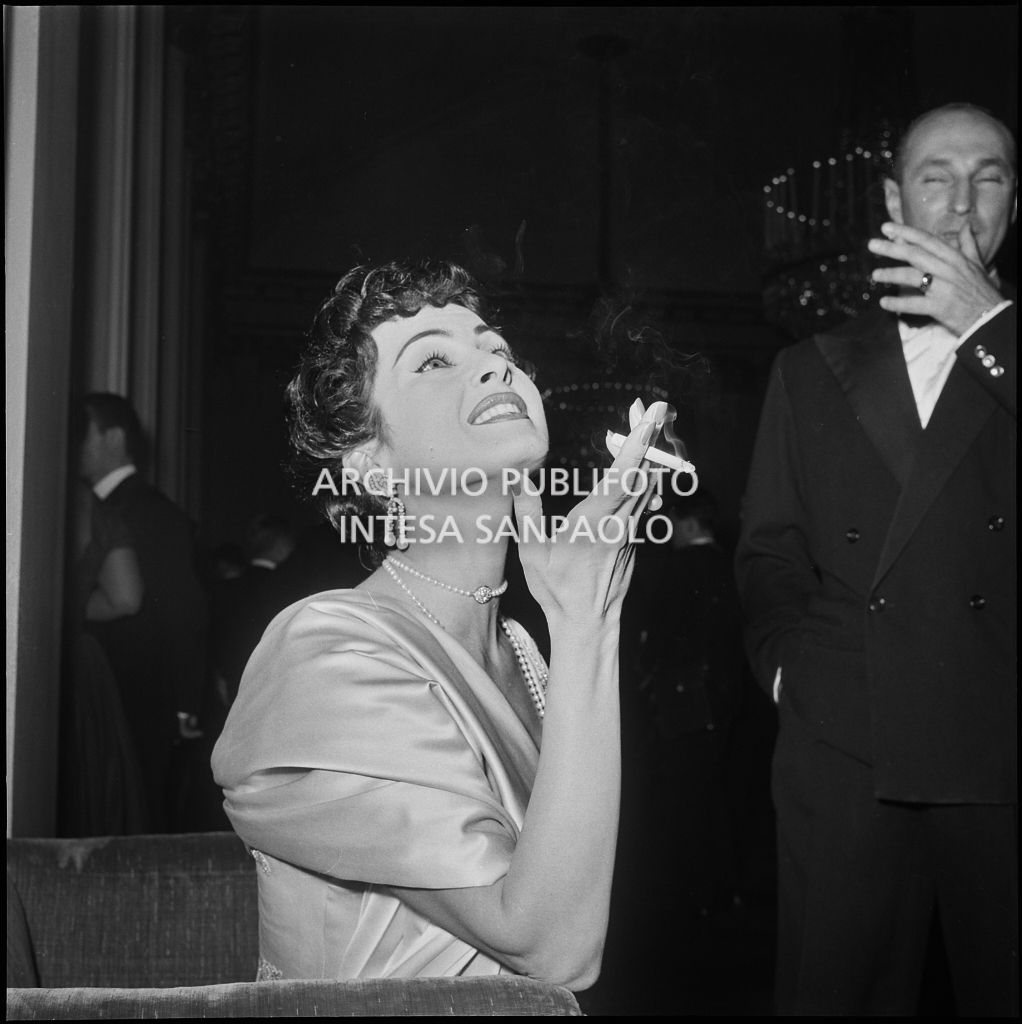 Silvana Pampanini, con la sigaretta in mano, nel foyer del Teatro alla Scala in occasione della serata inaugurale della stagione lirica 1956-1957 con l'opera "Aida" di Giuseppe Verdi, diretta da Antonino Votto, con la regia di Franco Enriquez