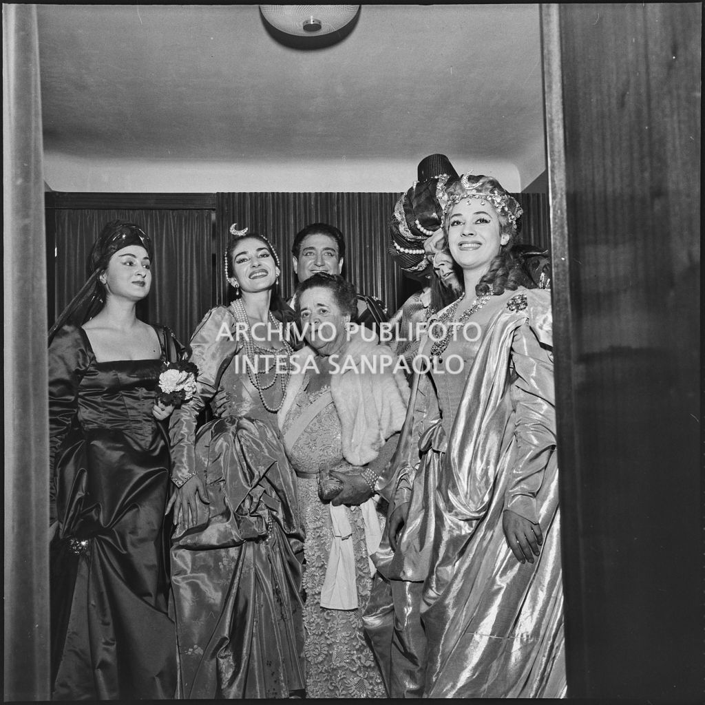 La soprano Maria Callas, in costume di scena, ritratta, tra le altre, con  la giornalista Elsa Maxwell al Teatro alla Scala in occasione della rappresentazione di "Ifigenia in Tauride"