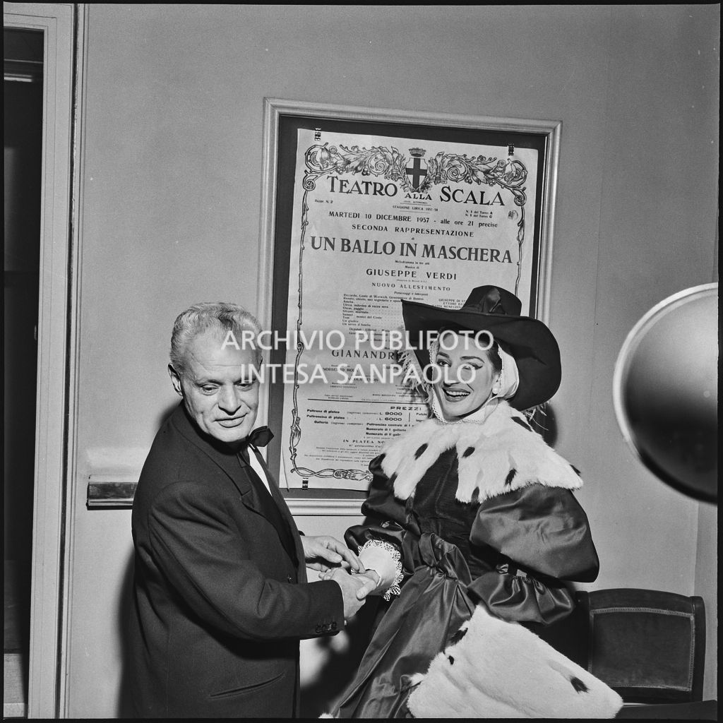 Il soprintendente del Teatro alla Scala Antonio Ghringhelli, e la soprano Maria Callas in costume di scena, ritratti in teatro davanti alla locandina di "Un ballo in maschera" la sera dell'inaugurazione della stagione lirica 1957-1958 con l'opera di Giuseppe Verdi, diretta da Gianandrea Gavazzeni e con la regia di Margherita Wallmann