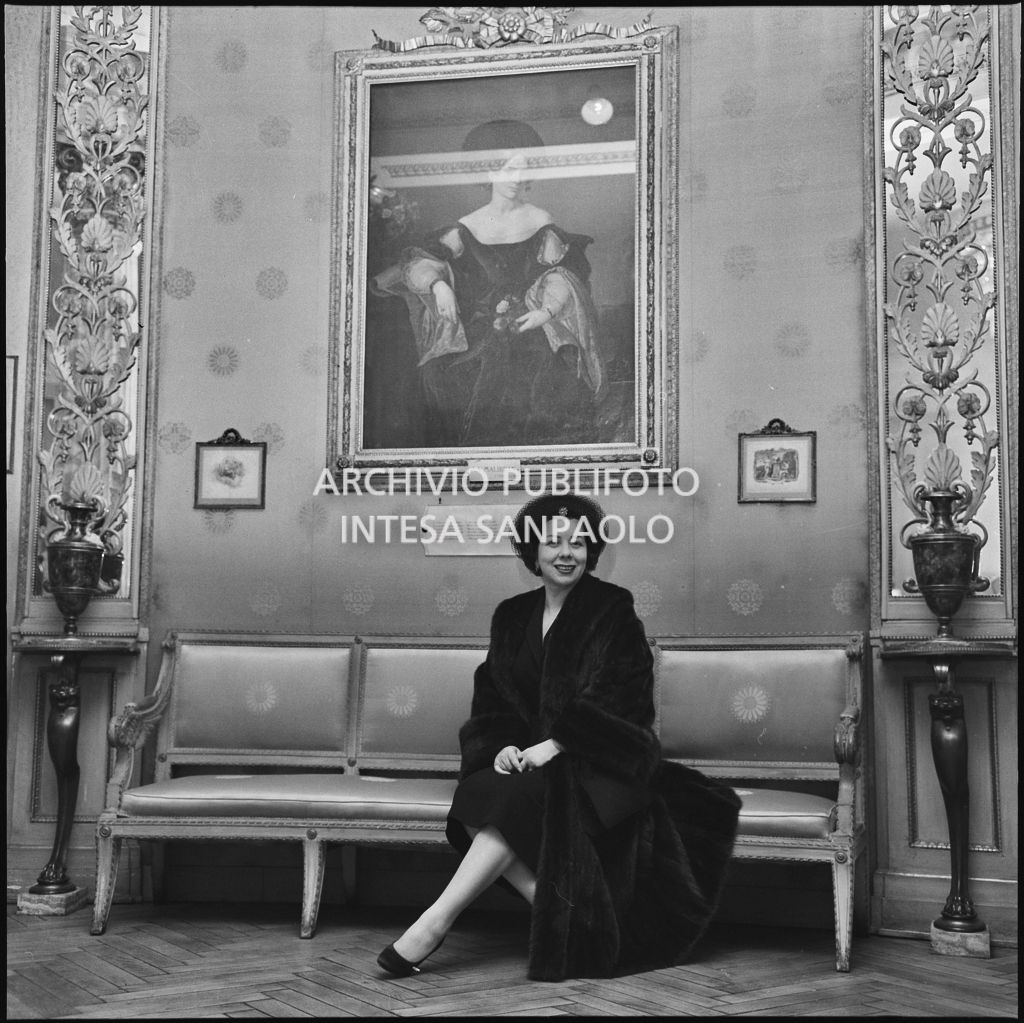 Il mezzosoprano Giulietta Simionato seduta sotto al ritratto di Maria Malibran al Teatro alla Scala in occasione della serata inaugurale della stagione lirica 1957-1958 con l'opera di Giuseppe Verdi "Un ballo in maschera", diretta da Gianandrea Gavazzeni e con la regia di Margherita Wallmann