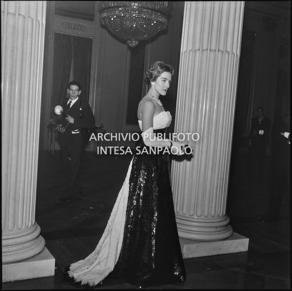 Marika Carniti, al Teatro alla Scala, in occasione della serata inaugurale della stagione lirica 1957-1958
				con l'opera di Giuseppe Verdi "Un ballo in maschera", diretta da Gianandrea Gavazzeni e con la regia di Margherita Wallmann; alle sue spalle un fotoreporter