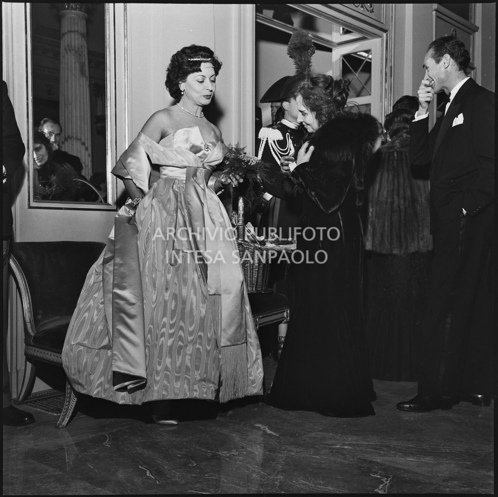 La baronessa Bianca Maria Hubner nel foyer del Teatro alla Scala, a fianco alla fioraia, in occasione della serata inaugurale della stagione lirica 1958-1959 con l'opera "Turandot" di Giacomo Puccini, diretta da Antonino Votto con la regia di Margherita Walmann