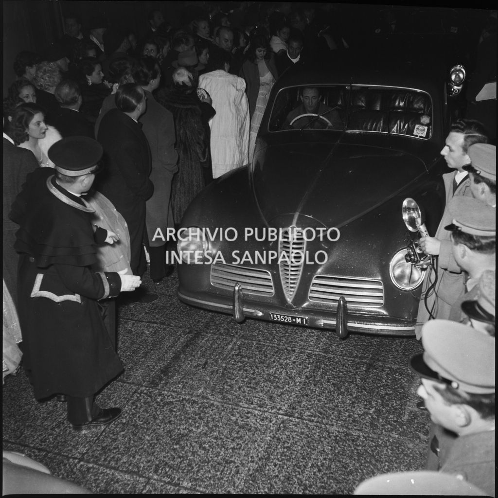Un'automobile tra gli spettatori affollati all'esterno del Teatro alla Scala, nella galleria delle carrozze, la sera dell'inaugurazione della stagione lirica 1952-1953 con l'opera "Macbeth", di Giuseppe Verdi, diretta da Victor de Sabata, con la regia di Carl Ebert