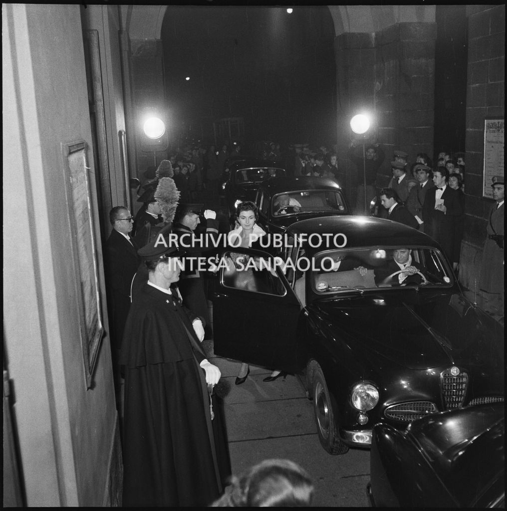 Automobili  nella galleria delle carrozze del Teatro alla Scala accompagnano gli spettatori alla serata inaugurale della stagione lirica 1954-1955 con l'opera "La Vestale", di Gaspare Spontini, diretta da Antonino Votto, con la regia di Luchino Visconti