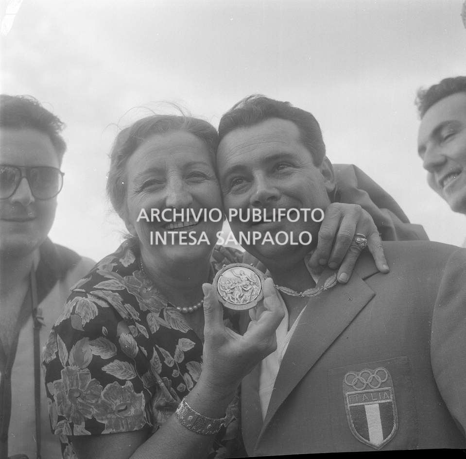 Una donna abbraccia Galliano Rossini, campione di tiro a volo italiano,  mostrando la medaglia d'argento conquistata nel tiro al piattello, XVII Olimpiade a Roma