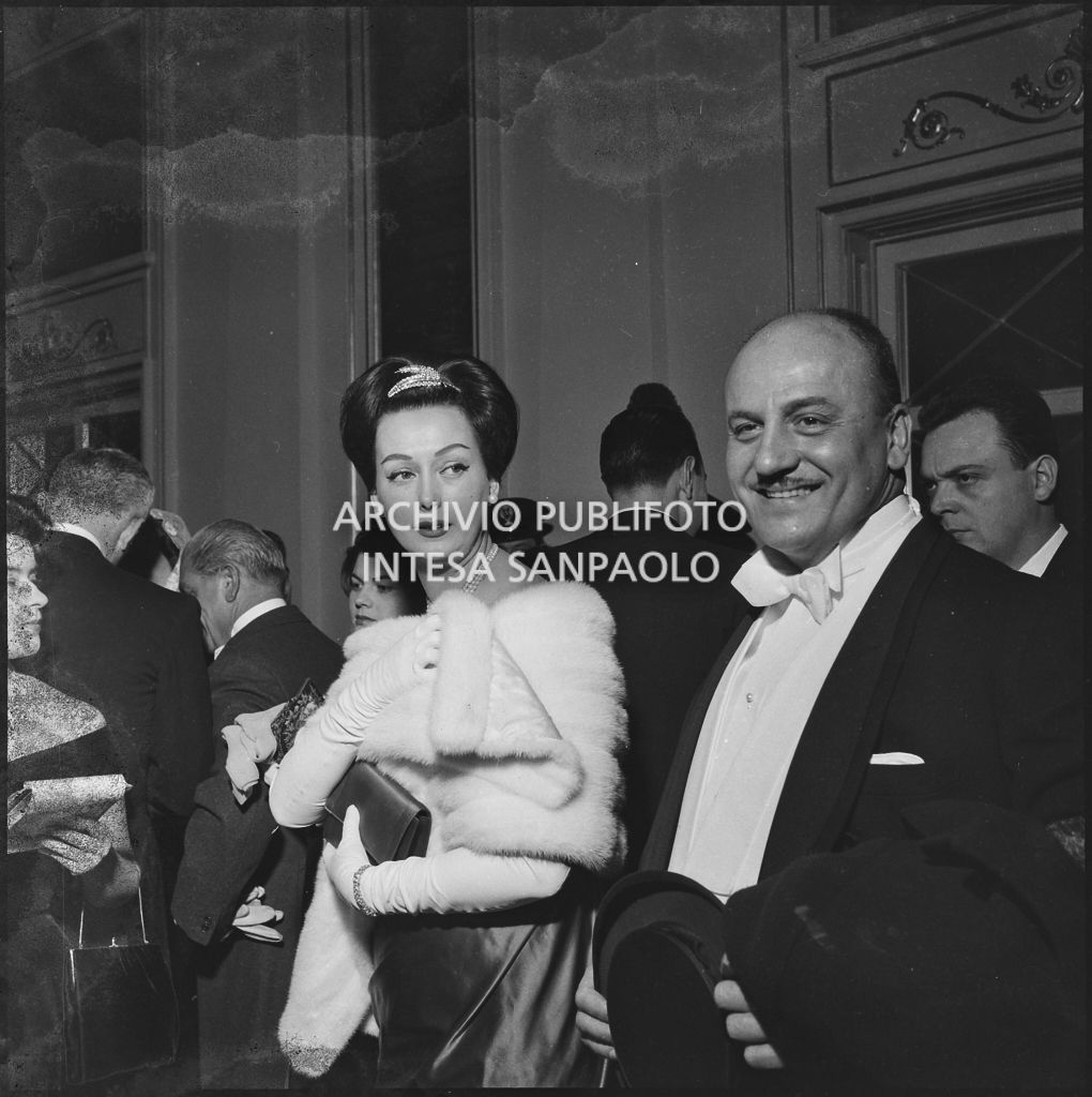 Lo stilista Pierre Balmain e Madeleine Kohler nel foyer del Teatro alla Scala in occasione della serata inaugurale della stagione lirica 1958-1959 con l'opera "Turandot", di Giacomo Puccini, diretta da Antonino Votto con la regia di Margherita Wallmann