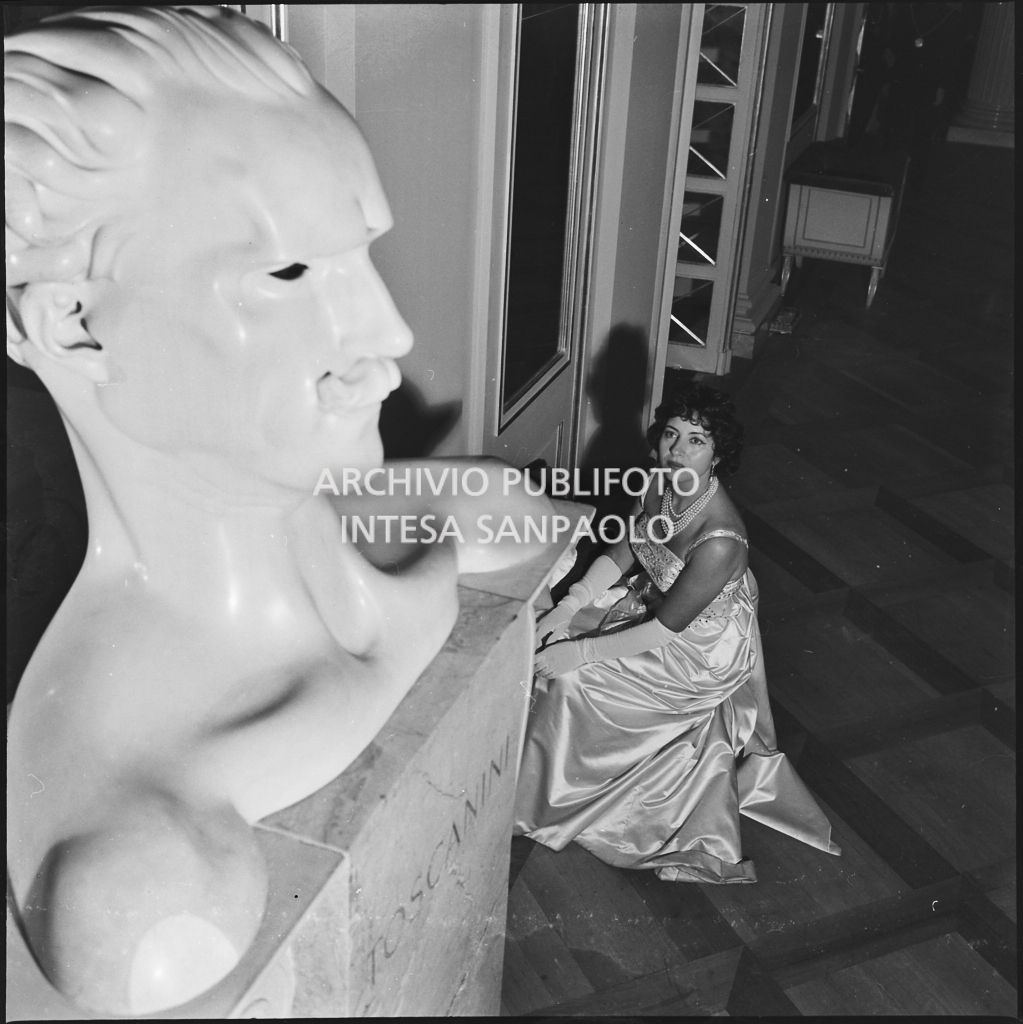 Il soprano Clara Petrella in posa accanto al busto di Arturo Toscanini al Teatro alla Scala in occasione della serata inaugurale della stagione lirica 1958-1959 con l'opera "Turandot", di Giacomo Puccini, diretta da Antonino Votto con la regia di Margherita Wallmann