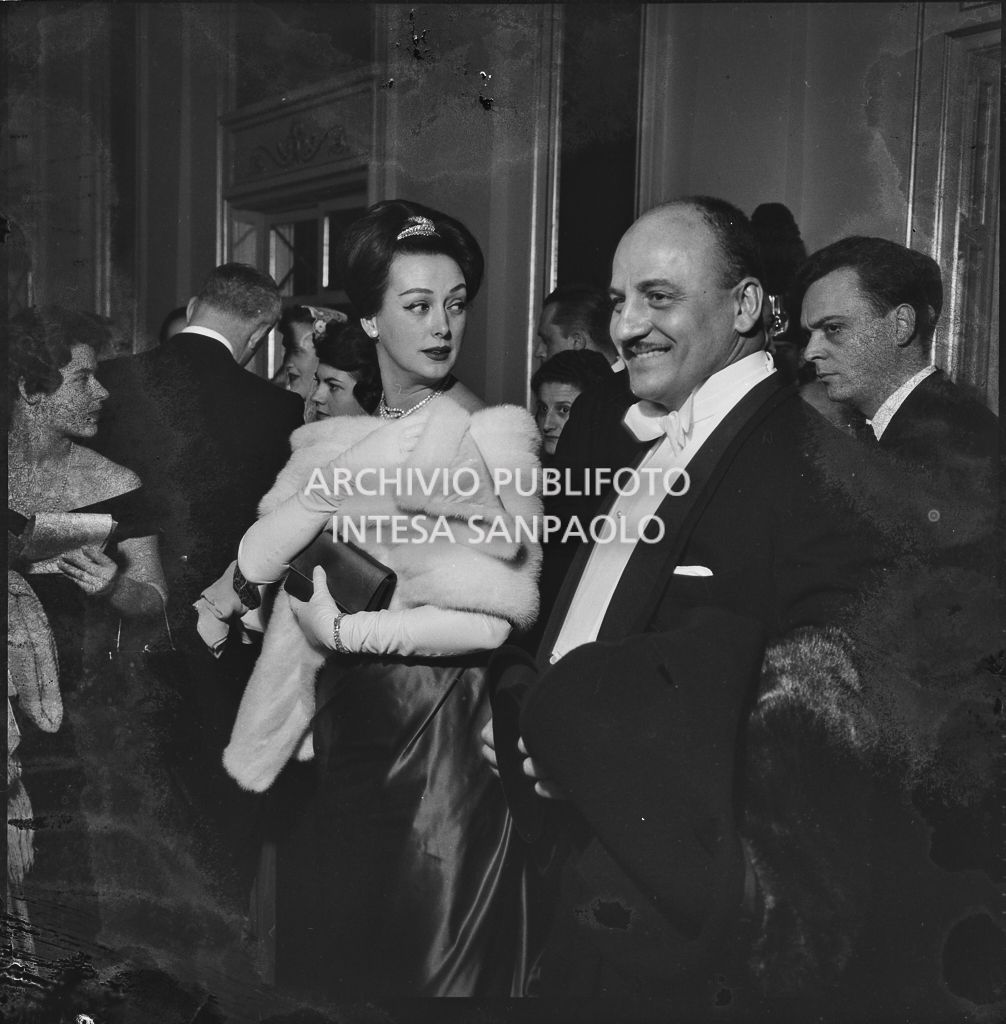 Lo stilista Pierre Balmain e Madeleine Kohler nel foyer del Teatro alla Scala in occasione della serata inaugurale della stagione lirica 1958-1959 con l'opera "Turandot", di Giacomo Puccini, diretta da Antonino Votto con la regia di Margherita Wallmann