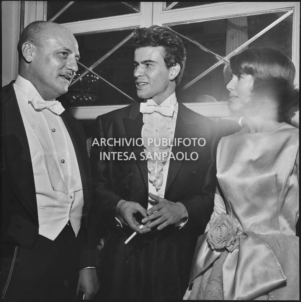 Lo stilista Pierre Balmain con gli attori Horst Buchholz e Myriam Bru nel foyer del Teatro alla Scala in occasione della serata inaugurale della stagione lirica 1960-1961 con l'opera "Poliuto" di Gaetano Donizetti, diretta da Antonino Votto con la regia di Herbert Graf