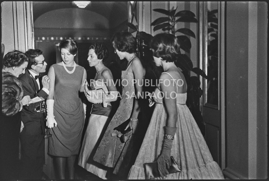 Le sorelle Caperano con la madre conversano con un fotografo al Teatro alla Scala in occasione della serata inaugurale della stagione lirica 1958-1959 con l'opera "Turandot", di Giacomo Puccini, diretta da Antonino Votto con la regia di Margherita Wallmann